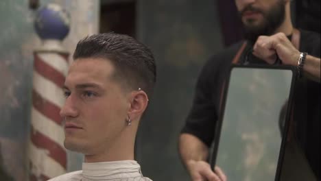Professional-hairdresser-shows-the-back-view-of-the-haircut-using-mirror-to-handsome-satisfied-male-client-in-a-professional