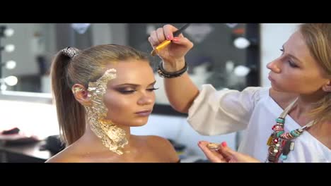 Makeup-artist-applying-golden-shiny-powder-on-the-model's-hair-using-special-brush.-Preparing-for-the-fashion-show.-Golden