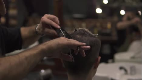 Close-Up-view-of-the-barber's-hands-performing-a-haircut-with-scissors-holding-a-hairbrush-in-his-hands.-Slow-Motion-shot