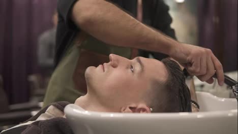 Close-Up-view-of-young-man-getting-his-hair-washed-by-and-unrecognizable-barber-in-a-barber-shot