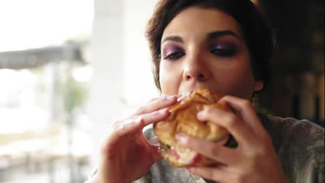 Close-Up-view-of-young-woman-biting-big-tasty-burger-in-cafe.-Slow-Motion-shot