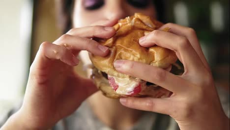 Close-Up-view-of-young-woman-biting-big-tasty-juicy-burger-in-cafe.-Slow-Motion-shot