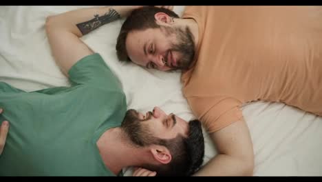 Portrait-of-attractive-bearded-gay-men-couples-lying-on-bed-together,-talking-and-caress-each-other