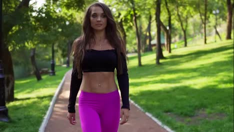 Smiling-female-trainer-in-short-sport-top-walking-in-the-park-after-intensive-training.-Fit-healthy-sport-woman-exercising-in
