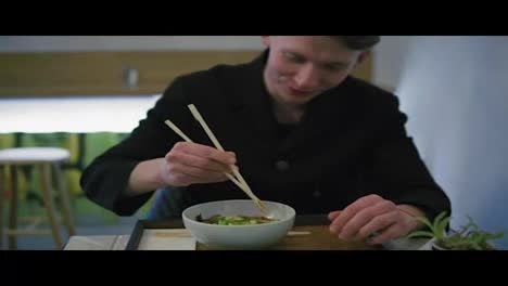 Close-Up-view-of-a-man-trying-to-eat-noodles-using-chopsticks.-Learning-how-to-hold-chopsticks.-Noodles-with-vegetables.-Dinner