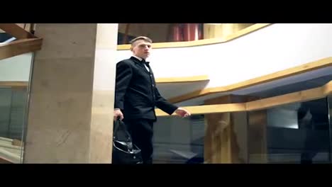 Young-businessman-in-a-suit-with-a-bowtie-is-going-down-the-stairs-holding-big-black-leather-bag.-Slow-Motion