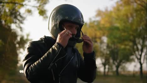 A-young-man-in-black-leather-jacket-and-helmet-wearing-sunglasses-while-sitting-on-his-motorcycle-preparing-to-start-his-journey