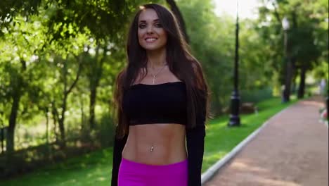Smiling-brunette-woman-in-short-sport-top-walking-in-the-park-after-intensive-training.-Fit-healthy-sport-woman-exercising-in