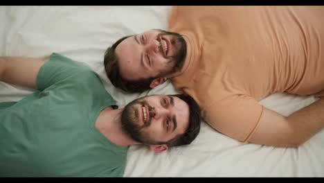 Portrait-of-attractive-bearded-gay-men-couples-lying-on-bed-together,-talking.-Top-view-footage