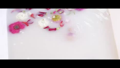 Close-Up-view-of-young-woman-bathing-in-milk-bath-filled-with-flowers-and-getting-up-with-her-eyes-closed.-Spa-and-skin-care
