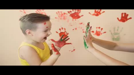 Young-mother-with-her-little-boy-are-mixing-colors-at-their-hands-yo-leave-beautiful-handprints-on-the-wall.-Mother-and-child