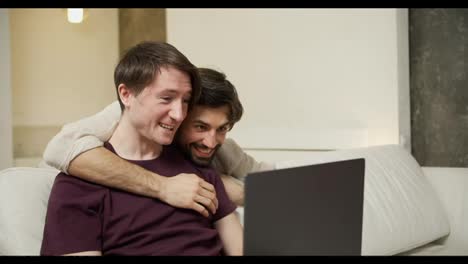 Happy-gay-couple-with-laptop,-a-man-came-to-hug-his-partner