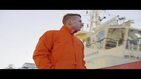 Hafenmeister-In-Orangefarbener-Uniform-Steht-Vor-Einem-Großen-Schiff-Im-Hafen-Und-Lächelt