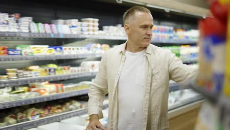 A-middle-aged-shot-visitor-chooses-products-in-the-dairy-section.-Product-viewing-and-selection.-Shopping