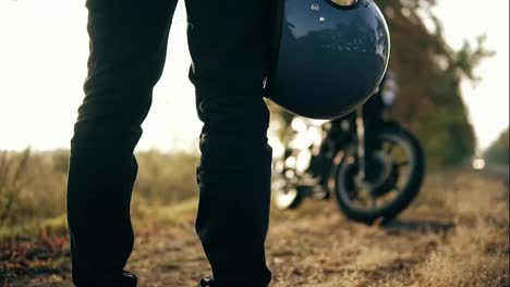Back-view-of-and-unrecognizable-man-in-black-jeans-and-leather-jacket-holding-his-helmet-in-his-hand-while-standing-by-his-cool