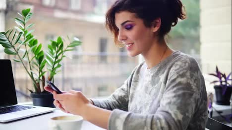 Close-Up-view-of-beautiful-young-woman-using-her-mobile-phone-in-cafe-and-smiling.-Woman-using-app-on-smartphone-in-cafe-drinking