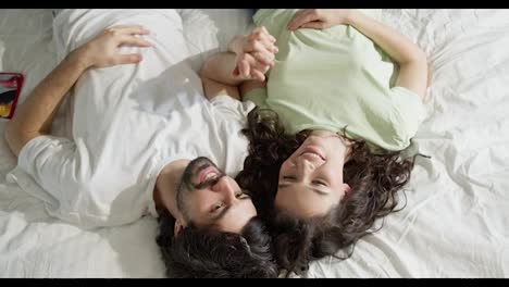 Young-couple-lying-on-bed,-they-are-happy-together,-top-view