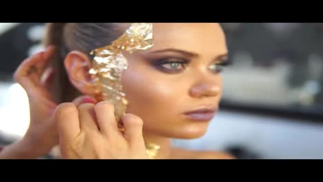 Close-up-shot-of-a-makeup-artist-applying-golden-shiny-pieces-of-metallic-paper-on-a-model's-face.-Preparing-for-the-fashion