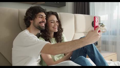 Cheerful-couple-taking-a-selfie-with-a-smartphone-at-room