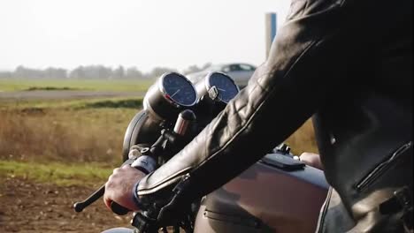 Side-view-of-a-man-in-black-helmet-and-leather-jacket-riding-motorcycle-on-a-asphalt-road-in-the-field.-Sunny-day