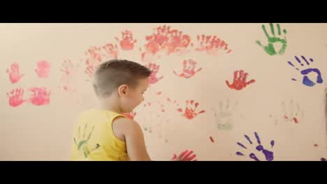 Happy-cute-little-boy-and-his-young-mother-are-having-fun-leaving-their-colorful-handprints-on-the-wall.-Young-happy-family