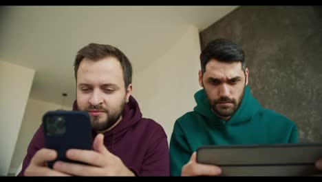 Young-gay-lgbtq-couple-using-mobile-phone-and-tablet-play-games-in-internet-together