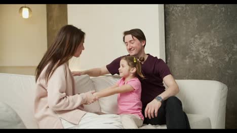 Young-family-with-small-daughter-sitting-on-sofa-talking-and-laughing-together-in-the-living-room