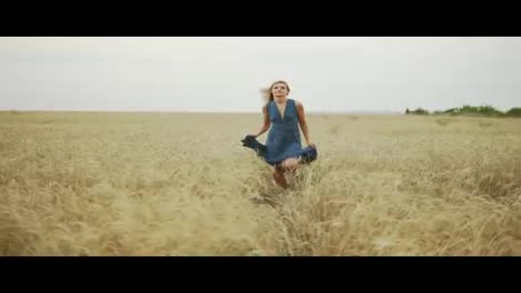 Handsome-young-woman-in-a-long-blue-dress-running-through-golden-wheat-field-looking-to-the-camera.-Freedom-concept.-Slow-Motion