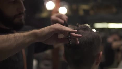 Close-Up-view-of-the-barber's-hands-performing-a-haircut-with-scissors-and-combing-the-client.-Slow-Motion-shot