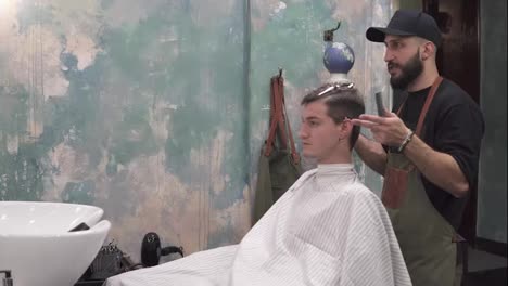 Portrait-of-and-adult-man-who-is-getting-his-haircut-by-a-bearded-barber-who-is-trimming-hair