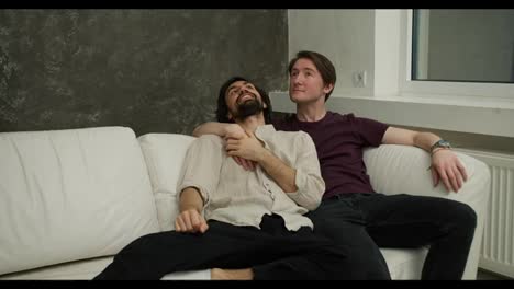 Two-men-couple-relaxing-on-the-couch,-happy-about-new-house