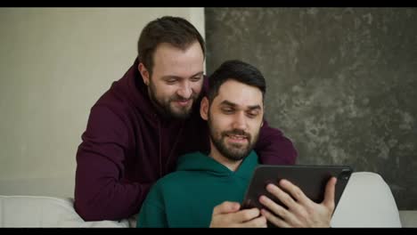 Fröhliche-Kaukasische-Männer-Schauen-Sich-Videos-Auf-Einem-Digitalen-Tablet-An,-Zeigen-Auf-Den-Bildschirm-Und-Lächeln