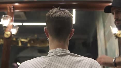 Back-view-of-a-young-man-getting-his-haircut-sitting-in-the-chair-at-the-barber-shot.-Barber-cuts-the-hair-of-the-client-with