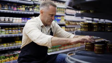 A-middle-aged-grocery-store-worker-controls-the-placement-of-goods-on-the-shelves.-Goods-control.-The-concept-of-working-in-a