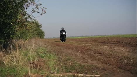 Front-view-of-a-man-in-black-helmet-and-leather-jacket-riding-motorcycle-on-a-country-road.-He-is-passing-by-the-camera