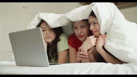 Three-best-friend-woman-on-bed-watching-horror-movie-on-laptop-with-shocked-expression-on-face