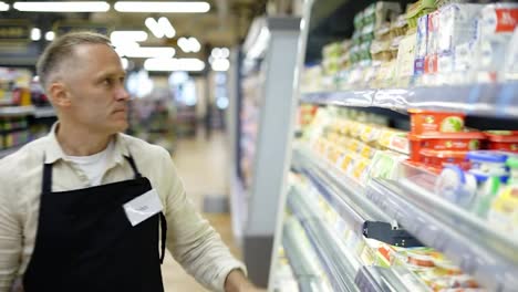 A-middle-aged-worker-in-a-grocery-store-adjusts-the-position-of-goods-on-a-shelf.-Dairy-department.-Inspection-of-goods,-work-in