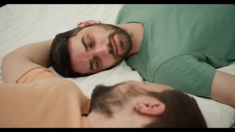 Portrait-of-attractive-bearded-gay-men-couples-lying-on-bed-together,-touching-face-with-romantic-feeling
