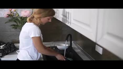 Young-pretty-housewife-washing-dishes-in-modern-kitchen-and-talking-to-someone.-FHD-shot
