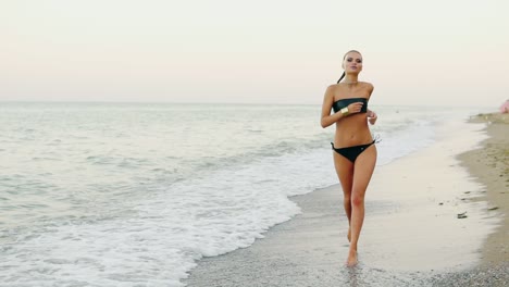 Young-attractive-woman-in-black-leather-swimsuit-running-by-the-sea-on-the-beach.-Her-ponytail-is-waving-in-the-wind-while-woman