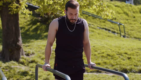 Athletic-lebanese-man-in-sportswear-practicing-dips-on-parallel-bars,-training-triceps-on-playground