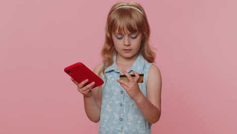 Child-girl-using-credit-bank-card-and-smartphone-while-transferring-money,-purchases-online-shopping