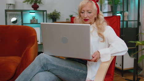 Senior-grandmother-woman-sitting-on-chair-closing-laptop-pc-after-finishing-work-in-room-at-home