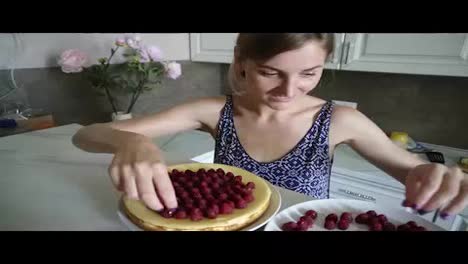 Young-smiling-woman-is-adoring-and-decorating-the-top-of-the-cake-with-raspberries-in-the-kitchen-at-home.-cheesecake-decorated