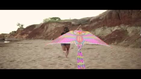Young-hipster-woman-releasing-colorful-kite-on-the-beach-in-the-evening.-Slow-Motion-shot