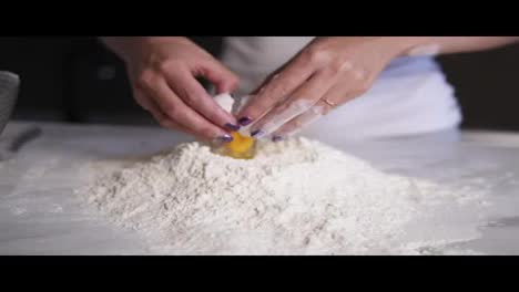 Close-Up-view-of-female-hands-breaking-the-egg-into-flour-on-the-kitchen-table.-Slow-Motion-shot