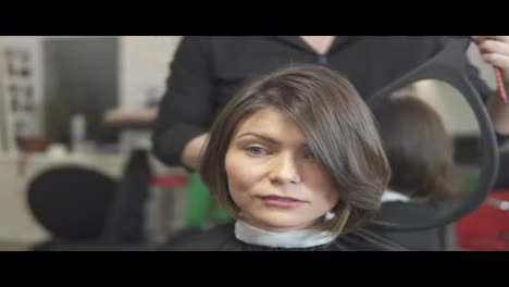 Professional-hairdresser-using-a-mirror-to-show-his-haircut-to-a-client.-Young-woman-getting-her-hair-dressed-in-salon