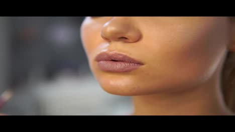 Close-Up-view-of-a-brush-with-golden-sparkle-gloss-applying-professional-makeup-on-the-model's-lips.-Lip-gloss-on-the-lips