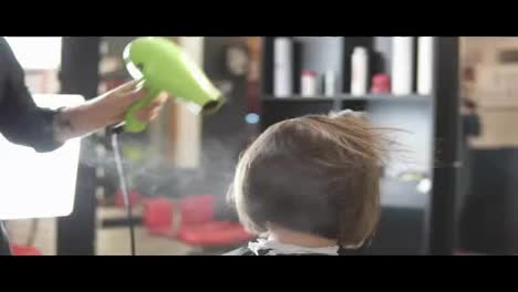 Young-woman-getting-her-hair-dressed-in-salon.-Hair-stylist-hairdresser-with-hair-dryer-applying-spray.-Beauty-salon.-shot-in