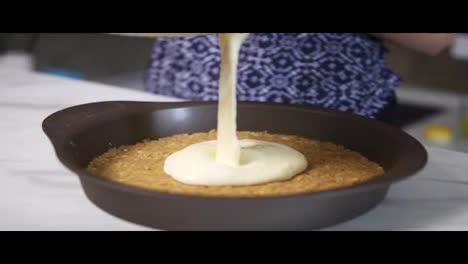 White-cream-cheese-topping-spread-on-the-a-biscuit-base-during-cheesecake-preparation.-Homemade-bakery.-Slow-Motion-shot